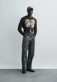 Brun stickad kofta med kaninmönster, ljusblå underställströja, grå denimjeans med vita kanintryck, svarta stövlar och blå keps.