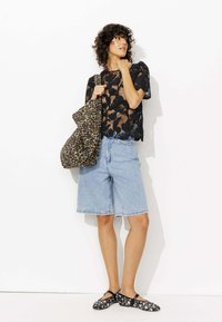 Top en dentelle noire avec motif floral, shorts en denim bleu clair, et chaussures slip-on noires à fleurs. Un grand sac en imprimé léopard complète la tenue.