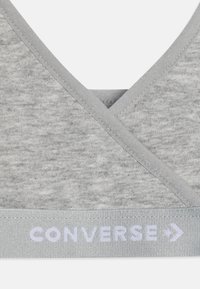 Grått stoff-bh med V-halsdesign, som har en myk tekstur og et kontrasterende elastisk bånd merket "CONVERSE" i hvitt.