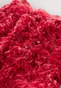 Červená textúrovaná látka s vrstveným, jemným materiálom a roztrúsenými kruhovými flitrami, ktoré vytvárajú bohatý, trojrozmerný vzhľad.