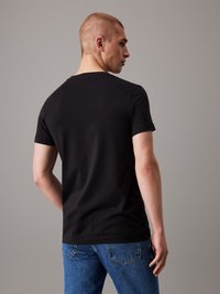 Black short-sleeve t-shirt with a round neckline, made of soft cotton, paired with blue denim jeans. Simple design with no patterns.