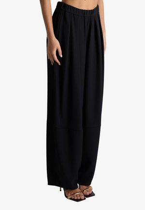 Donna che indossa pantaloni neri larghi abbinati a tacchi neri con punta quadrata e sottili cinturini dorati.