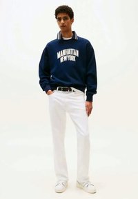 Mørkeblå genser med "MANHATTAN NEW YORK" trykket i hvitt, kombinert med hvite bukser og hvite joggesko. Har kragedesign.