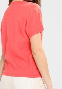 Korálová bavlněná tričko s krátkými rukávy, zaobleným výstřihem a uvolněným střihem. Hladká textura a jednoduchý design, žádné vzory ani akcenty.