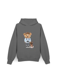 Szara bluza z kapturem z grafiką przedstawiającą niedźwiedzia w okularach, jasnoniebieskiej koszuli i spodniach, stojącego obok małego brązowego psa.