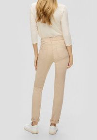 Pantalones ajustados beige hechos de tejido elástico, con una cintura alta y puños enrollados. Se pueden ver los bolsillos traseros y detalles de costura clara.
