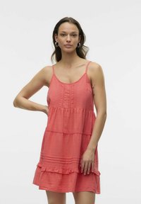 Vestido sin mangas en color coral con detalles de encaje y volantes en el dobladillo. Hecho de una tela texturizada, presenta un corsé ajustado y una falda suelta.
