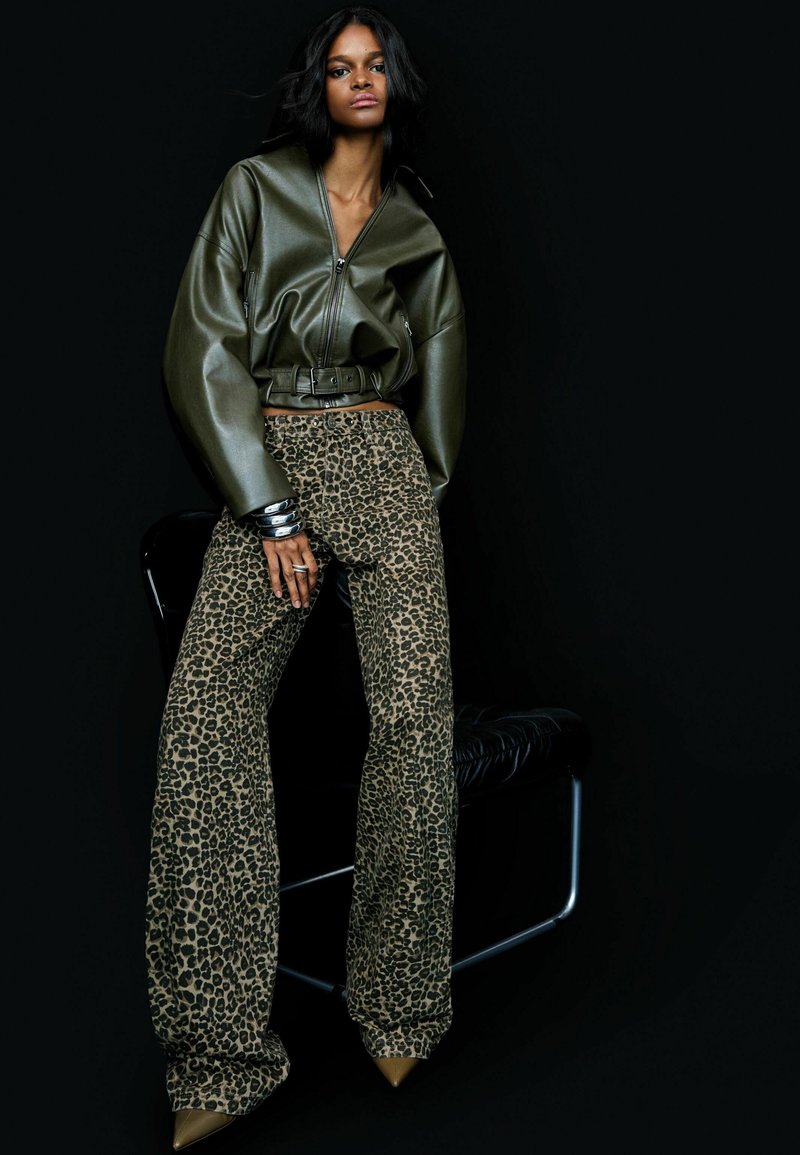 Oversized olijfgroene leren jas met een rits en een riem, gecombineerd met wijde leopardprint broeken en puntige nude hakken.