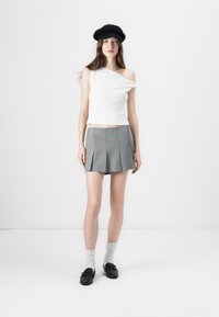 Top blanco de un solo hombro combinado con una mini falda de tablas gris. Un boina negra, zapatos negros y medias hasta la rodilla gris claro completan el conjunto.