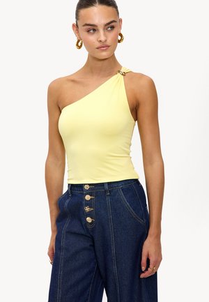 Haut asymétrique jaune avec une seule bretelle et un accent en anneau doré, associé à un pantalon en denim foncé taille haute avec des boutons décoratifs.