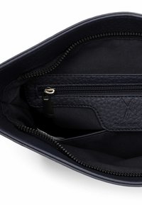 Wnętrze granatowej skórzanej torebki z zamykaną na suwak kieszenią, gładką teksturą i złotym metalowym suwakiem. Z boku znajduje się logo marki.