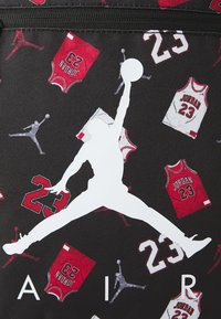 Schwarzer Stoff mit einem sich wiederholenden Muster von roten und weißen Basketball-Trikots und einem großen weißen Jumpman-Logo. Das Design enthält die Nummer 23.