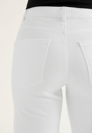 Zbliżenie na osobę noszącą dopasowane białe dżinsy z dwoma tylnymi kieszeniami oraz włożonym do środka czarnym topem.