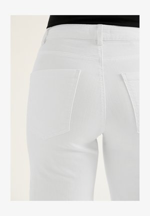 Zbliżenie na osobę noszącą dopasowane białe dżinsy z dwoma tylnymi kieszeniami oraz włożonym do środka czarnym topem.