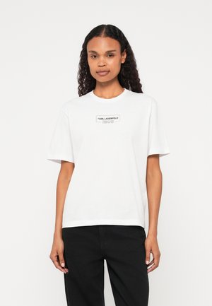 Bela bombažna majica s kratkimi rokavi, okroglim izrezom in črnim tiskanim logom "KARL LAGERFELD JEANS" na sprednji strani.
