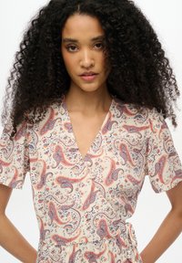 Vestido envolvente de paisley en crema con patrones en naranja y marino. Mangas cortas, escote en V y un lazo a la cintura. Tejido ligero y texturizado.