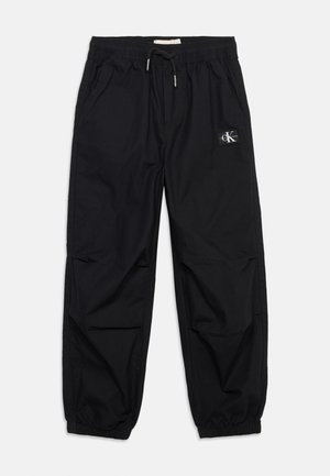 Black casual pants with elastic waist and cuffs, drawstring tie, side pockets, and a small logo patch on the right thigh.