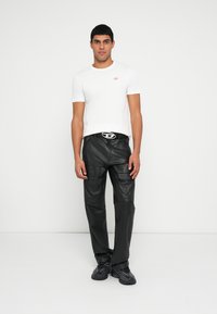 Biała koszulka z okrągłym dekoltem z małym czerwonym logo, w zestawie z czarnymi skórzanymi spodniami z kieszeniami na zamek oraz odważną srebrną sprzączką paska.