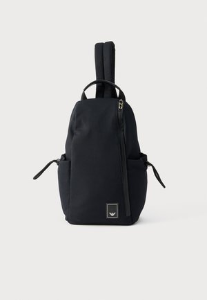 Sac à dos noir à côtes verticales, avec une poignée supérieure, deux bretelles rembourrées, des poches latérales et une fermeture éclair diagonale à l'avant.