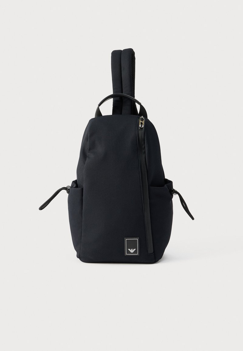 Μαύρο κάθετο ριγωτό σακίδιο πλάτης με χειρολαβή στην κορυφή, δύο επενδυμένους ιμάντες ώμου, πλαϊνές τσέπες και ένα διαγώνιο φερμουάρ μπροστά.