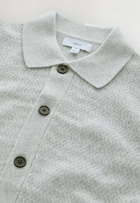 Hellgraue Strickjacke mit Fischgrätenmuster, Knopfverschluss und einer weichen, strukturierten Oberfläche. Verfügt über einen Kragen und dunkle Knöpfe.