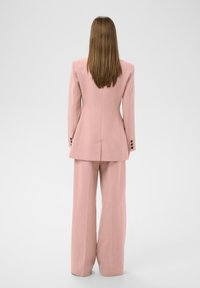 Rosa maßgeschneiderter Anzug mit strukturiertem, doppelt geknöpftem Blazer und weit geschnittenen Hosen. Mit Reverskragen und Knopfakzenten an den Bündchen.