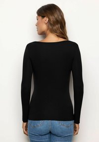 Top nero a maniche lunghe con una texture a coste e una scollatura ampia, abbinato a jeans di denim blu, visto da dietro.