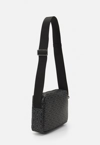 Czarna prostokątna torebka na ramię z wzorem logo, regulowanym materiałowym paskiem i gładką teksturą, z zamkiem błyskawicznym i minimalnymi akcentami.