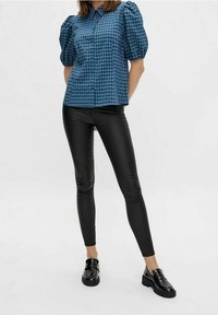 Blå rutad blus med puffärmar, kombinerad med tajta svarta leggings och glansiga svarta loafers. Tyget verkar slätt, lätt och väldefinierat.