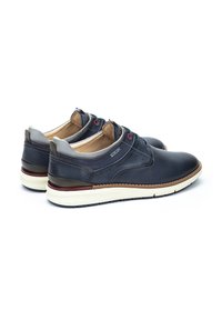 Zapatos de piel de color marino con detalles grises, diseño con cordones y suela blanca en contraste. Parte superior texturizada con perforaciones sutiles y ojales rojos.
