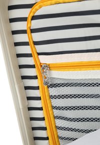 Intérieur en nylon rayé d'un sac de voyage, comportant des zips orange et blanc, une poche en maille, et une texture lisse avec une palette de couleurs claires.