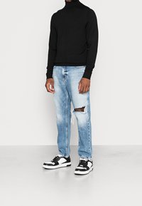 Pull à col roulé noir, jean bleu clair déchiré avec des détails usés, et baskets noires et blanches avec fermeture à lacets.