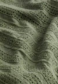 Tela verde oliva con patrones calados intrincados y bordados texturizados, creando una apariencia suave y en capas.