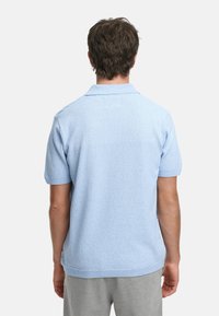 Lyseblå kortermet polo skjorte laget av teksturert stoff, med klassisk krage og ribbestrikkede mansjetter og hem. Bakside vist.