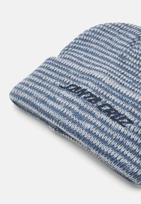 Strikket lue i blå og lyseblå striper med brettet mansjett. Har brodert tekst i svart på mansjettflaten.