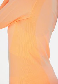 Pitkähihaiset paita kirkkaan oranssista kankaasta, jossa on hienovaraisia pystyribbausjuovia, esittelee sileää pintaa ja tiukkaa siluettia.