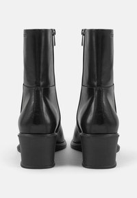 Černé kožené kotníkové boty s hladkou texturou, zaoblenou špičkou a blokovým podpatkem. Mají boční zip a minimalizované šití.