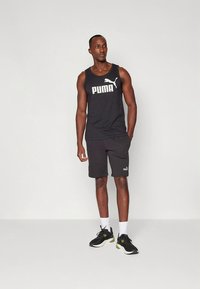 Svart linne med framträdande vitt "PUMA"-logotyp, kombinerat med svarta shorts med en liten logotyp samt svarta sportskor med gröna accenter.