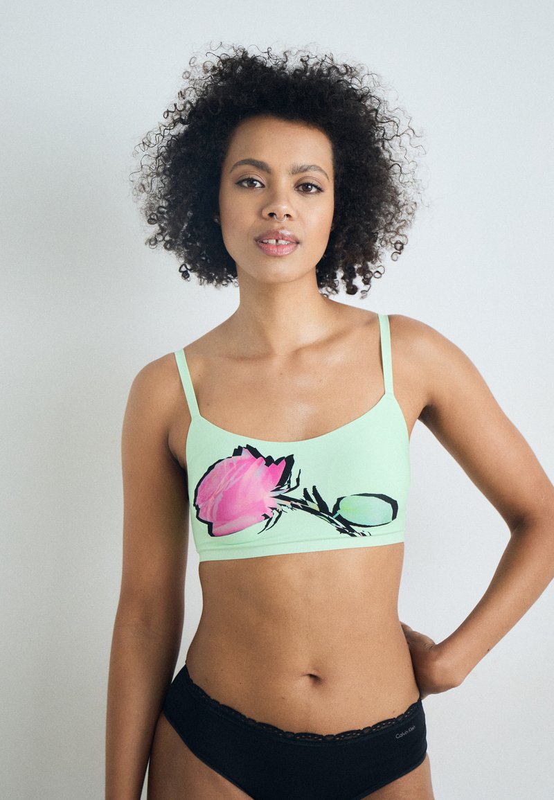 Myntgrön bralette med en stor rosa rosen-grafik, justerbara axelband och en slät textur; parat med svarta underkläder med spetsdetaljer.