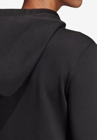 Hoodie noir à la texture douce, avec une capuche et une coupe décontractée. Le tissu semble lisse et légèrement extensible.