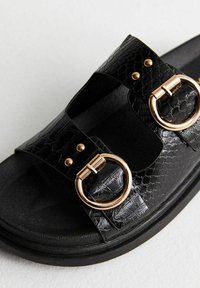 Sandales texturées noires avec deux larges brides, boucles rondes dorées et semelle noire profilée pour le confort.