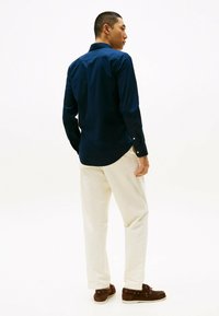 Chemise bleu marine à boutons avec des manches longues, complétée par un pantalon crème et des chaussures marron ; texture lisse et coupe décontractée.