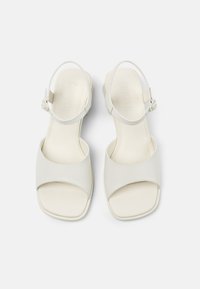 White leather sandals with an open toe design, adjustable ankle strap, and a low block heel. Smooth texture and minimalist style details.