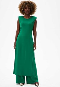 Groene midi-jurk met mouwloos ontwerp en zijsplit, gemaakt van een soepele stof. Gepaard met brede broekspijpen en gedessineerd schoeisel.