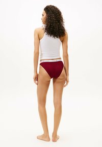 Mutande di cotone bordeaux con un elastico bianco in vita sul quale è stampato il nome del marchio "TOMMY HILFIGER". Il modello indossa una canotta bianca attillata.