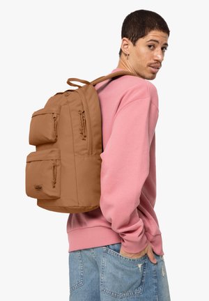 Mochila marrón con múltiples bolsillos con cremallera, hecha de un material duradero; llevada cómodamente sobre el hombro. Sudadera rosa suave en contraste.