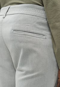 Pantalon de couleur gris avec une texture de tissu lisse, coupe slim et poche arrière avec une fente étroite. Fini avec une ceinture plate.