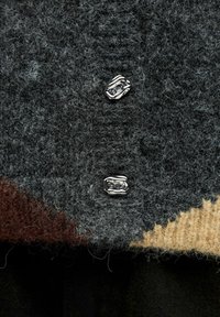 Wollpullover mit einer strukturierten grauen Oberfläche, ausgestattet mit zwei silbernen Knöpfen und einem farblich abgesetzten Muster in Braun und Beige am Saum.