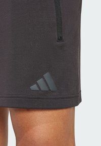 Sorte treningshorts laget av teksturert materiale, med et subtilt mønster og en grå Adidas-logo nederst til venstre.