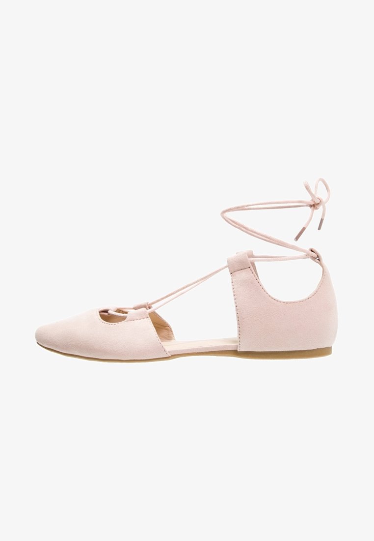 Chaussure de ballet plate rose clair avec bout pointu, côtés ouverts et brides autour de la cheville nouées en nœud.